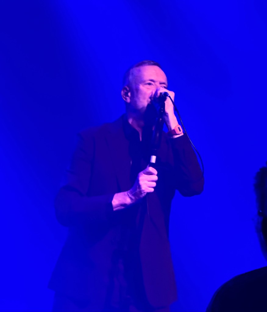 A singer performing on stage under blue lighting, holding a microphone.